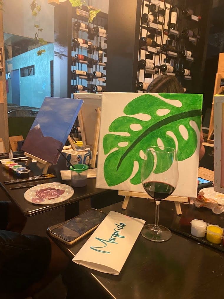 A monstera leaf painting beside a glass of wine